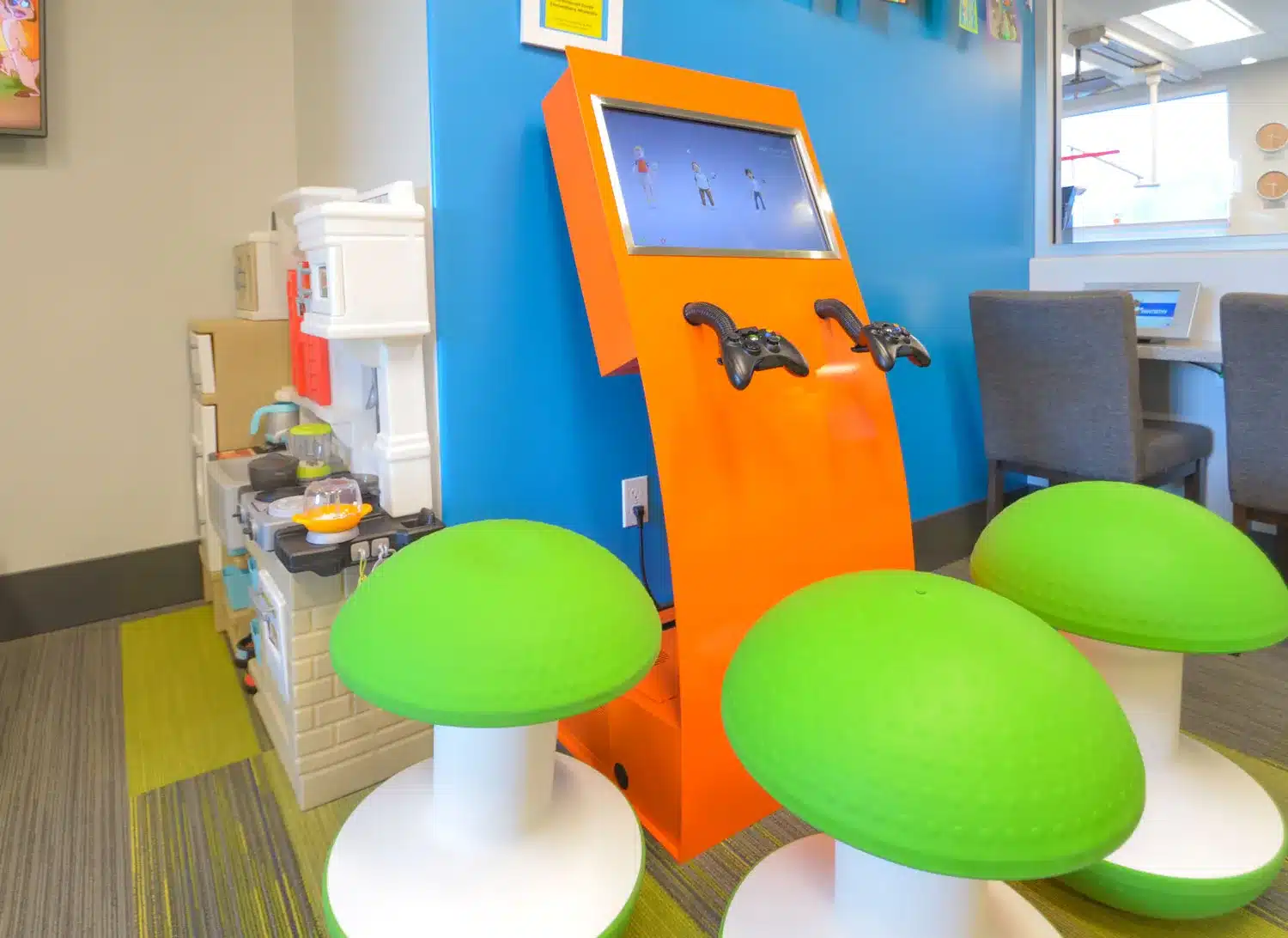 Colorful pediatric clinic play area with a game kiosk and mushroom seats